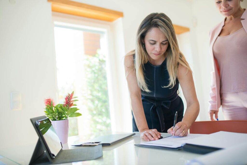 pexels-photo-8730015-8730015 Businesswomen signing a contract at a bright office desk with documents and tablet.